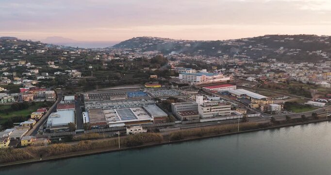 Aerial view of industrial buildings, roads and lush vegetation, contrasting with the dark water in Fusaro Lake, Bacoli, Campania, Italy.