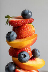 Stack of sliced strawberries, peaches, and blueberries on a light background with copy space