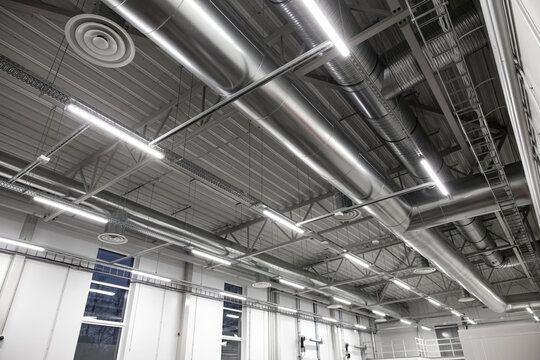 Interior view of a large industrial ceiling featuring exposed HVAC ducts, steel beams, and LED strip lighting. Clean design with visible infrastructure and copy space