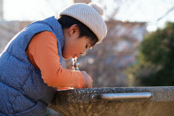Japanese boy hydrating at a park fountain during winter