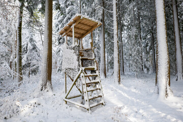 Snow-covered wooden hunting tower in a serene winter forest. Wide angle view, heavy snow cover, no people