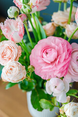 Beautiful bouquet of pink ranunculus and roses in a vase on a wooden table for romantic spring home...