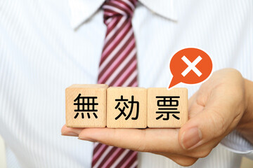 無効票を示す木製ブロックを持つ男性の手元。