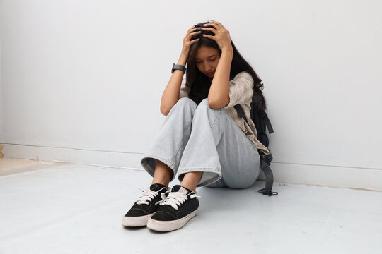 An Asian woman wearing casual clothes, sitting hunched over on the floor.
