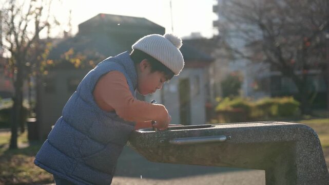 Japanese child quenching thirst at a public water fountain on a sunny day in the park