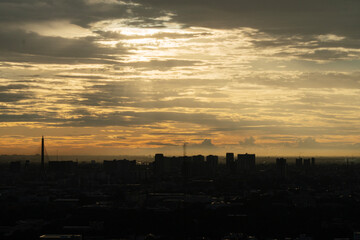 Fototapeta premium Dramatic golden sunset sky over Bangkok city silhouette with Rama VIII bridge. Beautiful sun rays shining through clouds on urban skyline architecture. Moody evening twilight landscape background.
