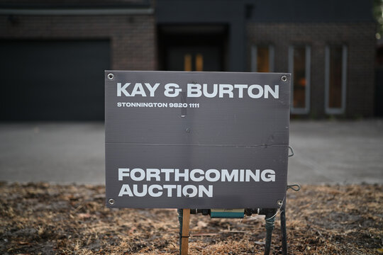 Kay and Burton real estate agent sign, promoting a forthcoming auction, in the yard of a suburban home early in the evening