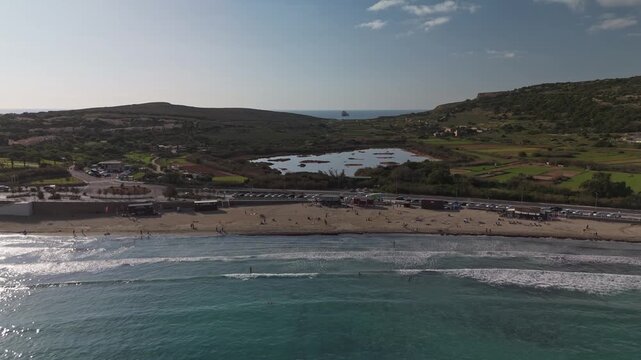 Sideways aerial view along the Ghadira Bay and the local nature reserve in Mellieha, Malta, highlighting the sandy Mediterranean beach and the surrounding natural reserve on a sunny winter day.