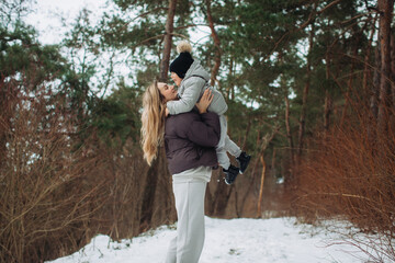 Obraz premium Mother lifting young child playing in winter forest