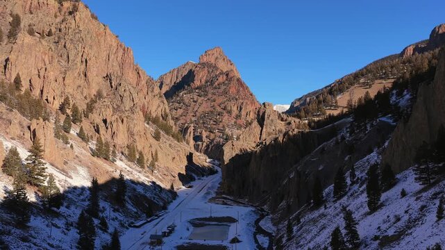 A cinematic aerial vista captures a sharp mountain peak rising between steep rocky canyon walls. Dramatic deep shadows and winter snow highlight the immense scale of this rugged mountain terrain.