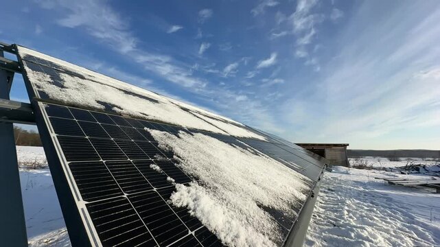 Winter timelapse of photovoltaic panels partially covered in snow. Clouds race west to east as the sun rises and gradually melts the snow, revealing dark glass rows beneath.