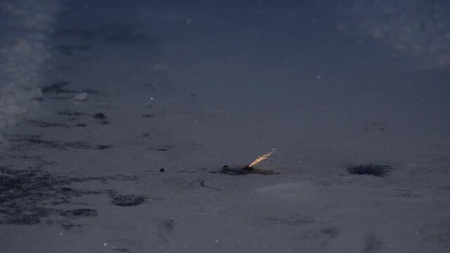 Adult lights tiny ground firework on snow using match, weak sparks and minimal effect