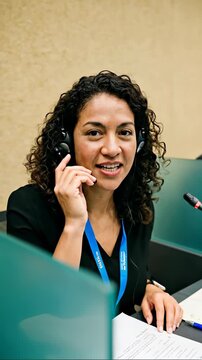 Professional female interpreter with curly hair wearing a headset and smiling while working in a simultaneous translation booth