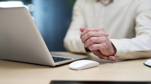 Close-up of businessman holding wrist in pain while working on computer mouse in office. Male employee massages sore hand suffering from carpal tunnel syndrome or repetitive strain injury at workplace