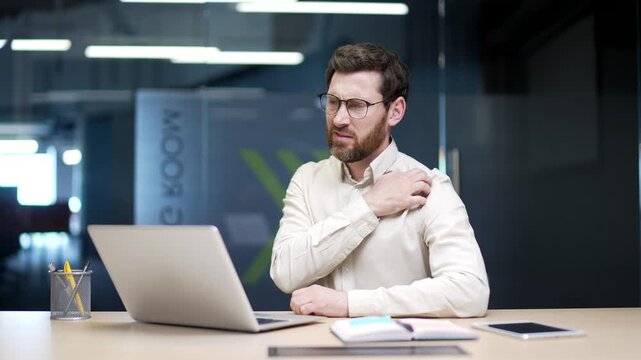 Businessman sitting at desk in office scratches his skin, suffering from itch or pruritus. Male employee reacts to allergy, mosquito bite, stress, or skin irritation, feeling discomfort while working.