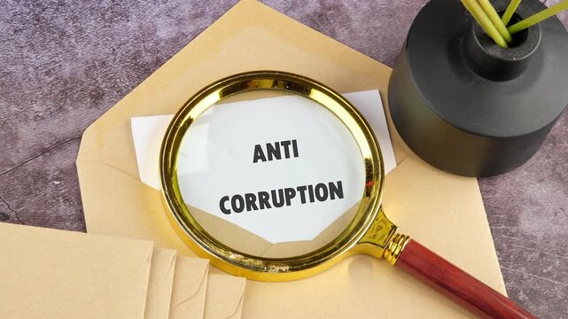 A magnifying glass slowly reveals the full phrase Anti Corruption on a piece of paper, set against a plain background with an envelope and a small vase