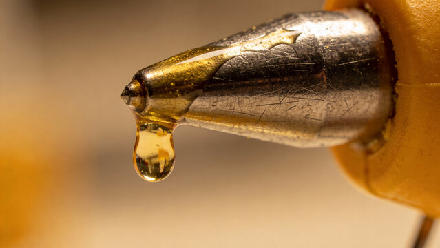 Macro Shot of Hot Glue Dripping from Gun Nozzle with Golden Light