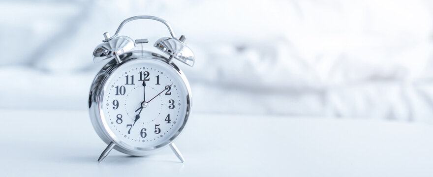 A clock indicates the time on a table in a bedroom setting. The soft background suggests morning activities are about to begin, with natural light entering the room.