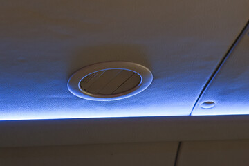 Calm interior passenger cabin showing overhead panel with blue led light strip and round speaker grille creating relaxing flight atmosphere for comfortable journey