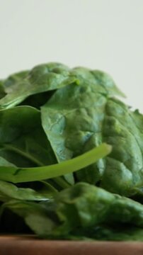 Fresh baby spinach leaves arranged on a wooden cutting board with a bright white background