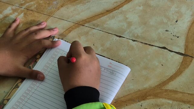 A girl student's hand is writing a story in a notebook in classroom