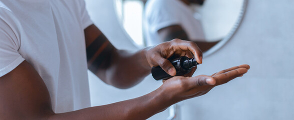 A man stands in a bathroom putting a skincare product on his palm. He is focused on his reflection in the mirror while preparing for his day ahead.