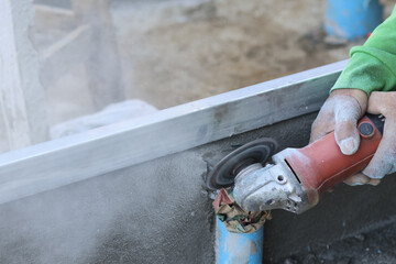 Close up shot worker hands using red angle grinder cutting blue pvc pipe with flying dust having concentrated feeling in construction site