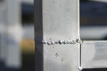 Closeup of sturdy silver metal frame with rough welded joint showing industrial texture and construction detail in confident strong style under bright daylight with blurred background focus