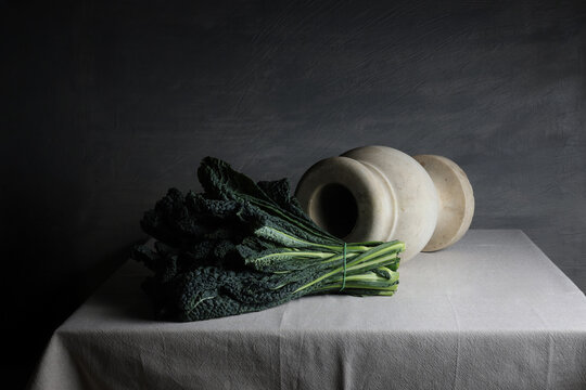 Cavolo nero e vaso in marmo bianco su tavolo in lino, composizione sobria ed essenziale