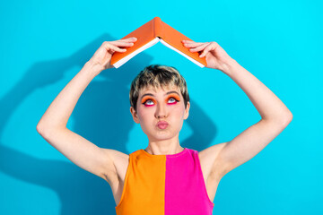 Young woman balances an orange book over her head a vibrant fashion portrait against a bright blue...