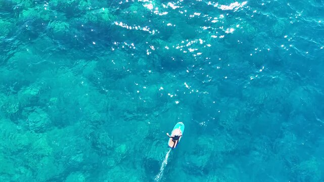 Aerial view of a person hydrofoil surfing over the clear, blue ocean waters under a bright sky, creating a mesmerizing scene, Hawi, Hawaii, United States.