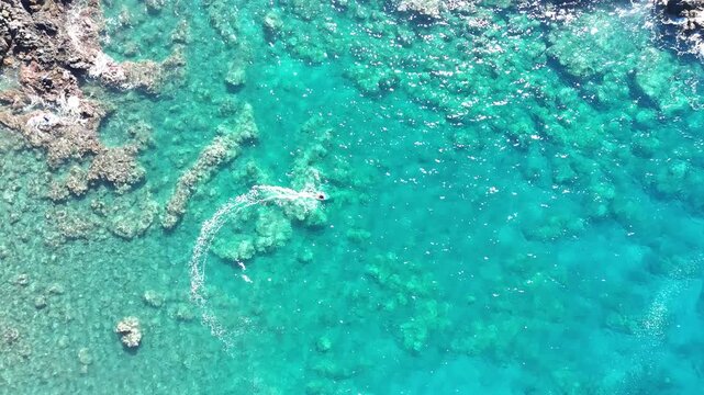 Aerial view of a person hydrofoil surfing over the clear, blue ocean waters under a bright sky, creating a mesmerizing scene, Hawi, Hawaii, United States.