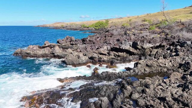 Aerial view of turquoise ocean meeting the rugged, dark rocky coastline under a clear blue sky, Hawi, Hawaii, United States.