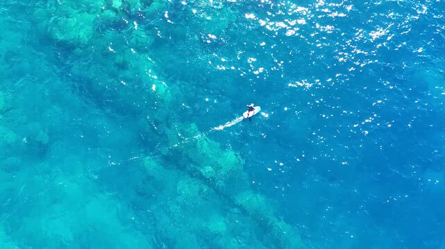 Aerial view of a person hydrofoil surfing over the clear, blue ocean waters under a bright sky, creating a mesmerizing scene, Hawi, Hawaii, United States.