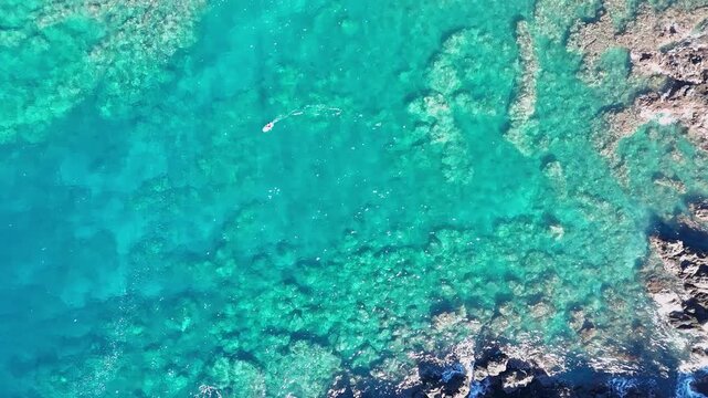 Aerial view of a person hydrofoil surfing over the clear, blue ocean waters under a bright sky, creating a mesmerizing scene, Hawi, Hawaii, United States.