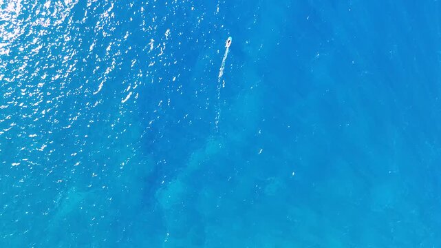 Aerial view of a person hydrofoil surfing over the clear, blue ocean waters under a bright sky, creating a mesmerizing scene, Hawi, Hawaii, United States.