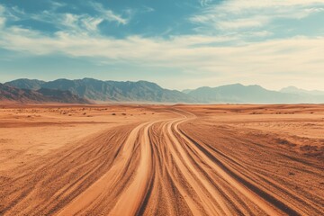 Desert road winding through sandy dunes under partly cloudy sky with distant mountain range creating serene and expansive landscape view