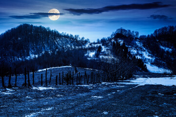 rural landscape of carpathian mountains in early spring under dark sky at night. snow covered hill with barbed wire fence in full moon light. inner strength to overcome fear, loneliness in darkness © Pellinni
