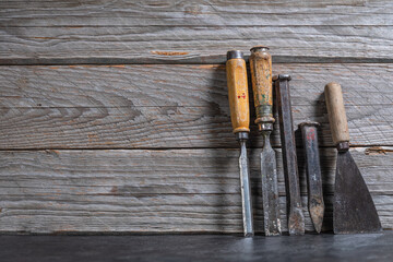 Side view of a rustic wooden wall with chisels, metal chisels, and a putty knife leaning on the right, leaving space for text on the left
