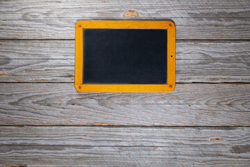 Top-down view of a small blank vintage chalkboard with wooden frame centered at the top on a rustic gray wooden table
