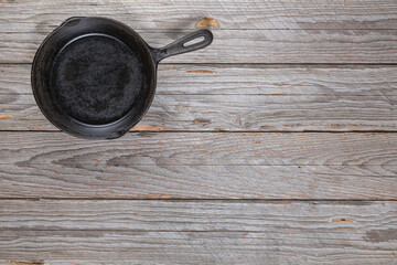 Top-down view of a small cast iron skillet with iron handle in the top-left corner on a rustic gray wooden table
