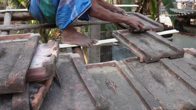 Worker installing traditional clay roof tiles on village home