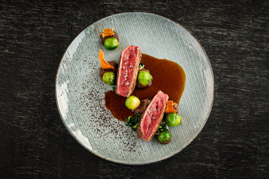 Top view of a steak and Brussel sprouts main course at a fine dining restaurant with gravy and garnish with a dark background