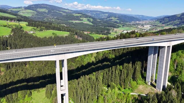 Aerial view of the Lavanttal bridge, with a verdant forest beneath its towering supports and cars moving across, Wolfsberg, Carinthia, Austria.