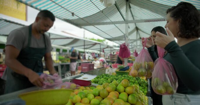 Female customer walking away from outdoor street market holding fruit bag and waving goodbye after local food purchase