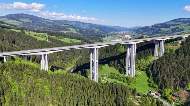 Aerial view of the Lavanttal bridge stands tall amidst lush green forests and rolling hills under a bright blue sky, Wolfsberg, Carinthia, Austria.
