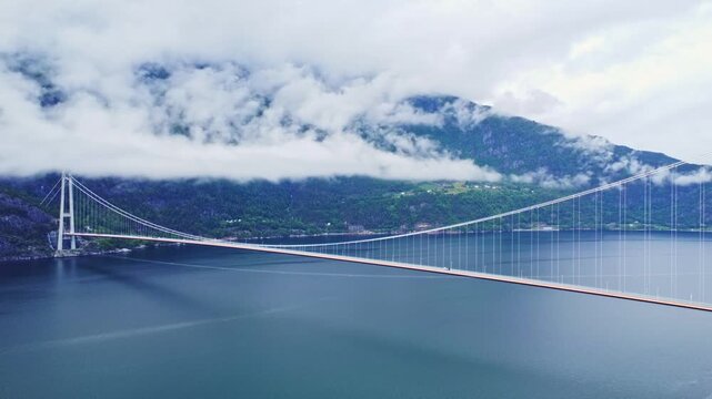 Aerial view of the Hardangerbrua bridge stretching across the water, with mountains partially obscured by clouds in the background, Bergen, Vestland, Norway.