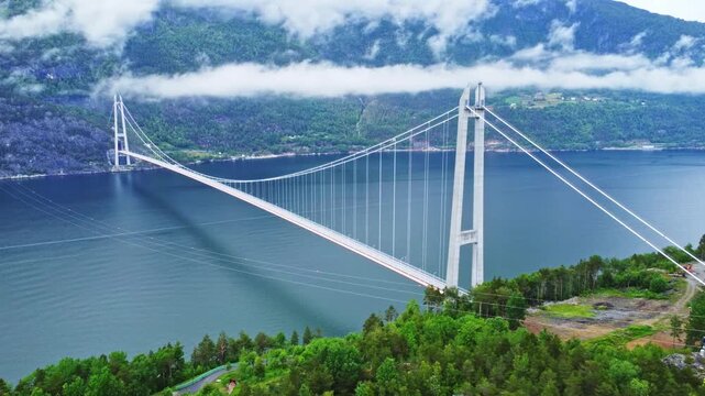 Aerial view of the majestic Hardangerbrua bridge spanning across the tranquil fjord waters beneath mist-shrouded mountains, Bergen, Vestland, Norway.