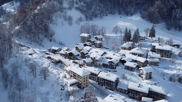 Aerial view of snow-covered buildings nestled among snow-laden trees, creating a serene winter landscape, Balme, Piedmont, Italy.