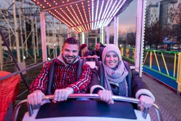 Happy couple enjoying night roller coaster ride at amusement park